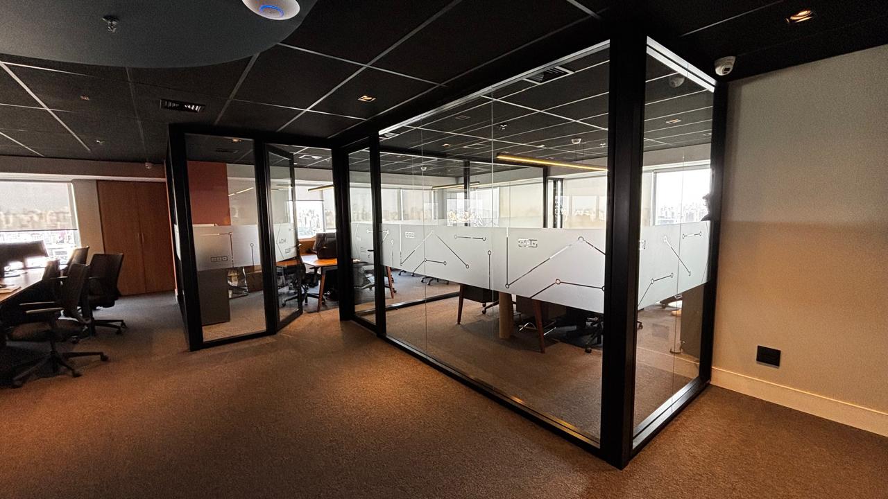 Sala de reunião com divisórias de vidro, perfis pretos e faixa de privacidade