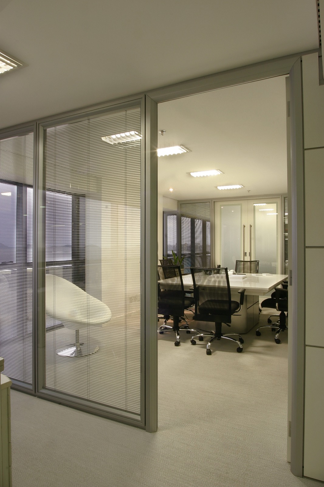 Sala de reunião com divisórias de vidro, persianas e perfis claros em projeto Formi